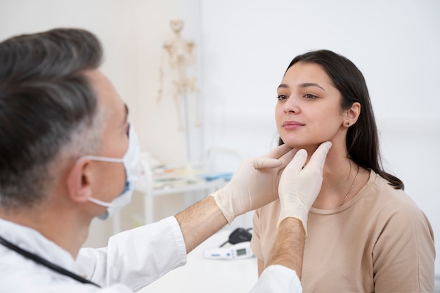 Medical provider wearing gloves gently examining a female patient’s neck during a routine consultation in a clinical setting.