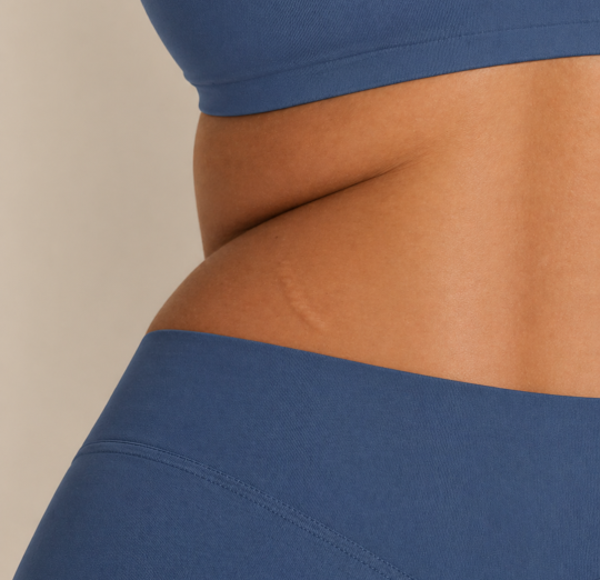 Close-up of a woman’s midsection wearing matte blue sports bra and high-waisted leggings against a neutral background