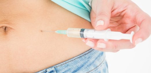 Woman injecting weight loss medication or supplement into her abdomen, close-up view of torso in jeans and light top.